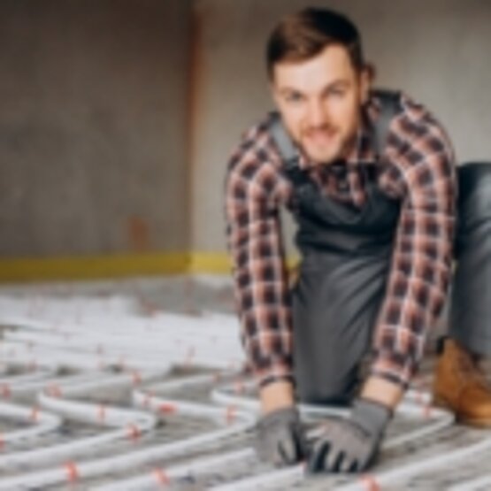 Handwerker kniet auf dem Boden und montiert Heizrohre einer Fußbodenheizung.